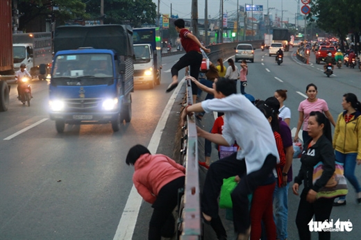 Cùng một đoạn dải phân cách nhưng người thì chui, người thì leo để băng qua đường trong làn xe lớn đang lao tới ngay trên quốc lộ 1A, Q.12, TP.HCM - Ảnh: NGỌC PHƯỢNG