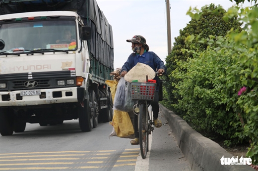 Một người dân đi xe đạp kế bên dải phân cách giữa những chiếc xe container để mưu sinh ngay trên QL1A, Q.12, TP.HCM - Ảnh: NGỌC PHƯỢNG