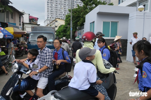 Tại Trường THCS Chi Lăng, quận 4, TP.HCM, một số phụ huynh đón con đi học về sáng 22-8 không đội nón bảo hiểm cho mình cũng như cho con trẻ - Ảnh: T.T.D.